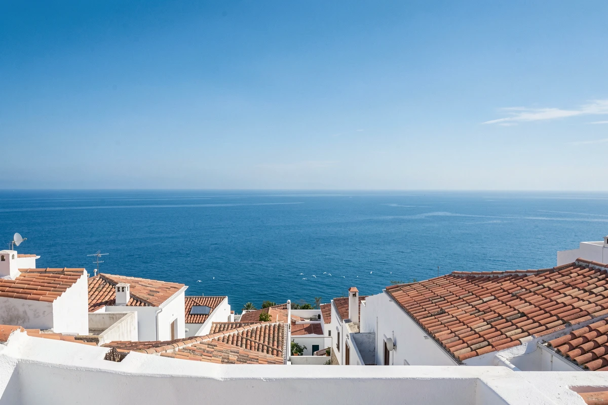 Ville côtière méditerranéenne avec ciel et mer azur vifs vus depuis une terrasse avec des toits en tuiles et des mouettes